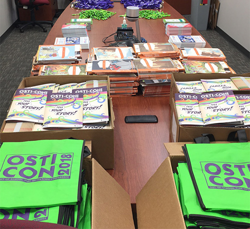 A photo of 2018 OSTI-CON conference paraphenelia including the program and branded tote bags.